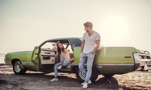 ロマンチックなカップルはビーチでグリーンのレトロな車に近い立っています。ハンサムなひげを生やした男とビンテージ クラシックカーと魅力的な若い女性。愛の物語. - 写真・画像
