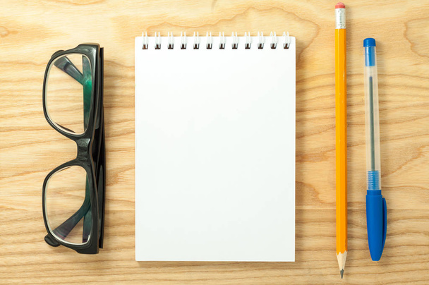 Vista superior del cuaderno en blanco espiral abierto, gafas, bolígrafo y lápiz sobre fondo de escritorio de madera
 - Foto, Imagen
