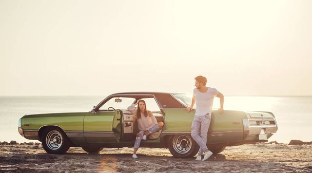 Romantic couple is standing near green retro car on the beach. Handsome bearded man and attractive young woman with vintage classic car. Love story. - Valokuva, kuva