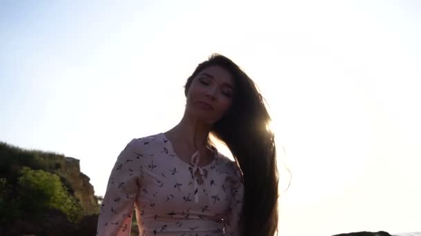portrait de Adorable fille brune caucasienne en robe rose clair jouer avec ses longs beaux cheveux à l'heure du lever du soleil
. - Séquence, vidéo
