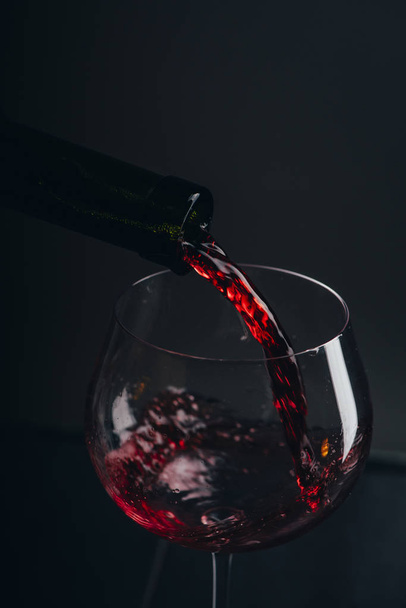 Red wine pouring in wine glass over black background. Closeup of red wine splashing in wineglass in restaurant. Wine tasting. - Zdjęcie, obraz