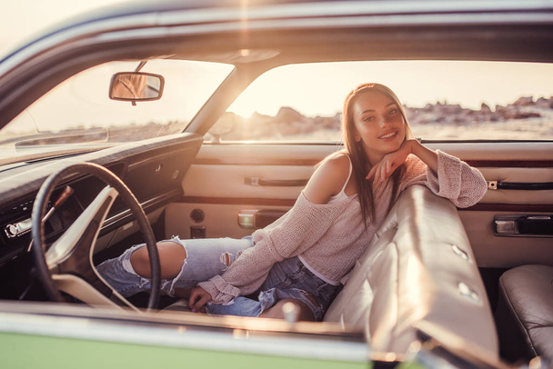 Attractive young woman is sitting in green retro car on the beach. Vintage classic car. - Foto, Bild