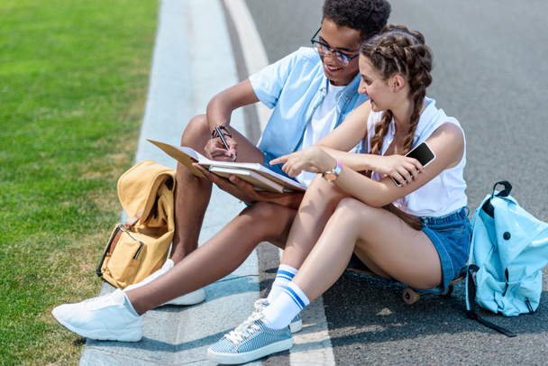 multiethnic teenage boy and girl studying together in park - Фото, изображение