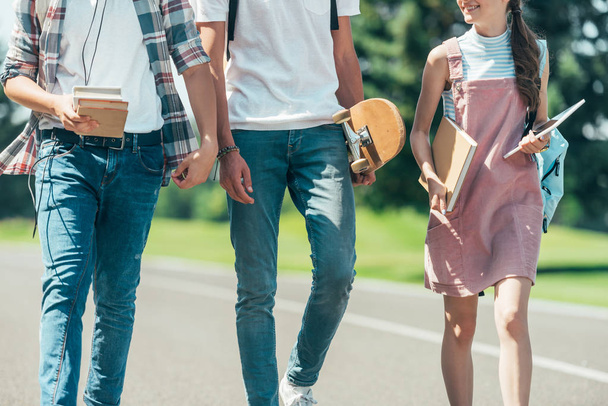 cropped shot of teenage students with books, digital tablet and skateboard walking together in park - Fotografie, Obrázek