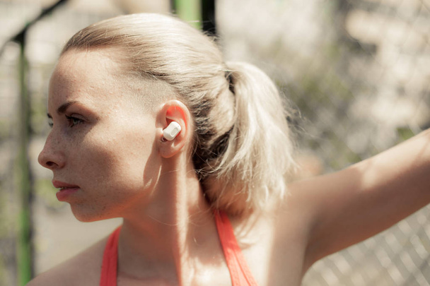 Mujer Fitness Escuchando Música en Auriculares Inalámbricos, Haciendo Ejercicios de Entrenamiento en la Calle. Auriculares Bluetooth de estilo deportivo
 - Foto, Imagen