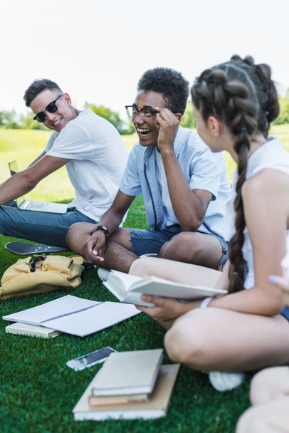happy multiethnic teenage students smiling while studying together in park  - Фото, изображение