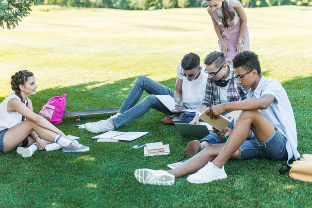 wieloetniczny nastoletnich uczniów studiuje się z książkami i laptopa w parku - Zdjęcie, obraz