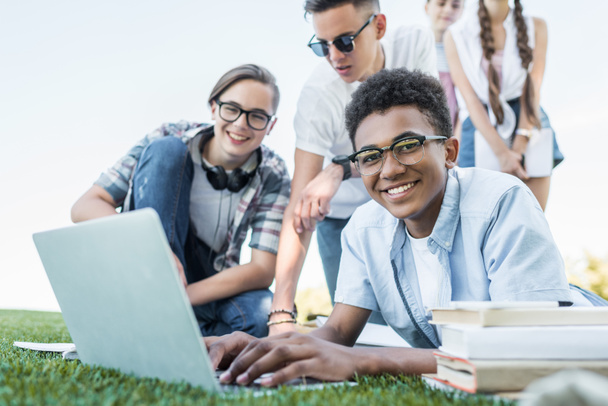 happy multiethnic teenagers using laptop and studying in park  - Photo, Image