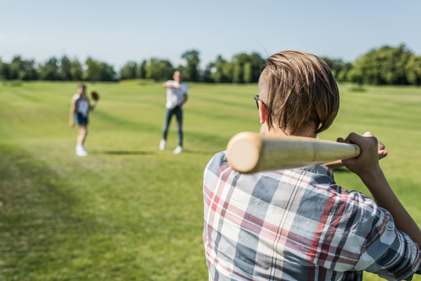 back view of teenage boy playing baseball with friends in park - Фото, зображення