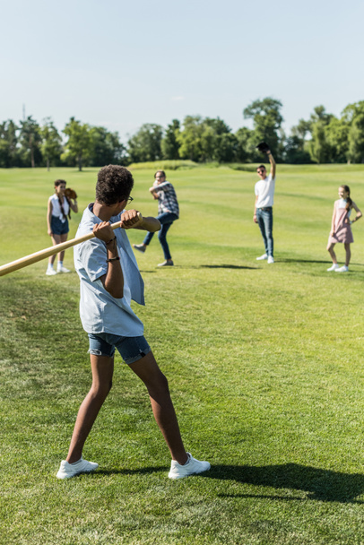 niño afroamericano jugando béisbol con amigos adolescentes en el parque
 - Foto, imagen