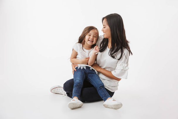Picture of happy young asian woman mother with her little girl child daughter sitting isolated over white wall background. - Φωτογραφία, εικόνα