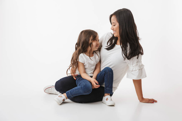 Image of cute young asian woman mother with her little girl child daughter sitting isolated over white wall background. - 写真・画像