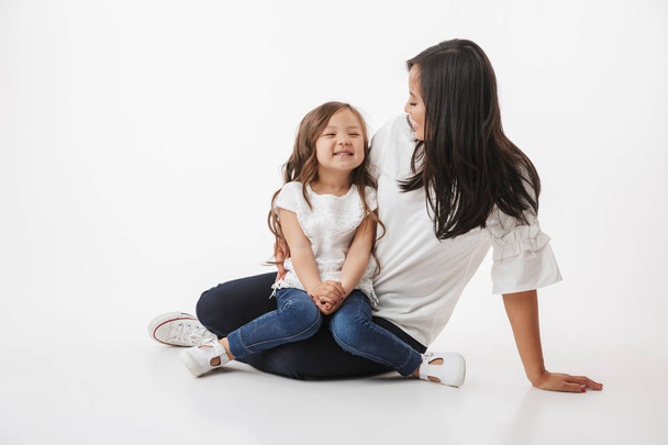 Image of cute young asian woman mother with her little girl child daughter sitting isolated over white wall background. - Valokuva, kuva