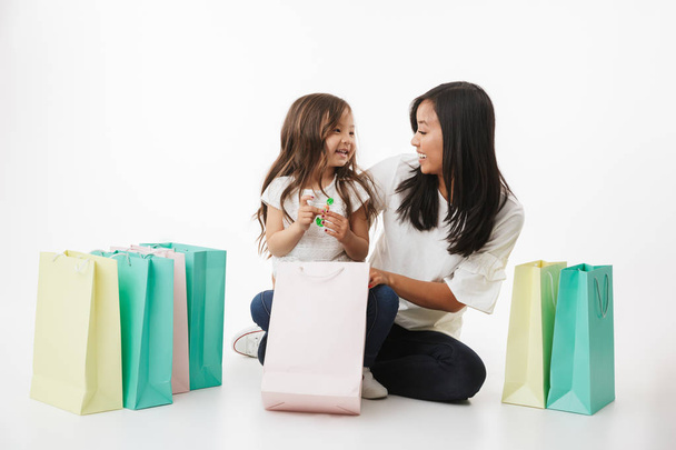 Image of happy young asian woman mother with her little girl child daughter isolated over white wall background with shopping bags. - Foto, afbeelding