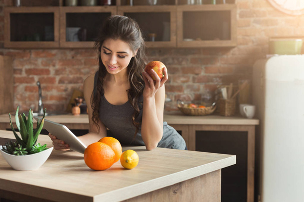Happy young woman eating fruits in kitchen - Photo, Image