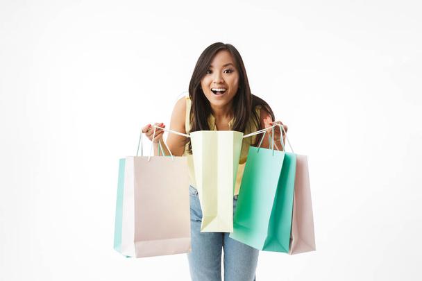 Image of excited young asian woman isolated over white wall background with shopping bags. - Foto, imagen