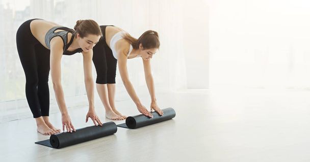 Sportliche Frauen rollen Matten nach Yoga-Training in leichtem Fitnessstudio auf - Foto, Bild