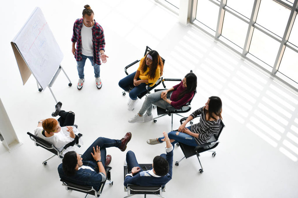 Grupo de empresários sentados em círculo ouvindo, questionando e prestando atenção a uma apresentação de um colega
 - Foto, Imagem
