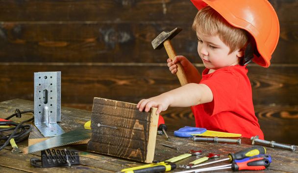 Toddler on busy face plays with hammer tool at home in workshop. Kid boy play as handyman. Handcrafting concept. Child in helmet cute playing as builder or repairer, repairing or handcrafting - Foto, Bild
