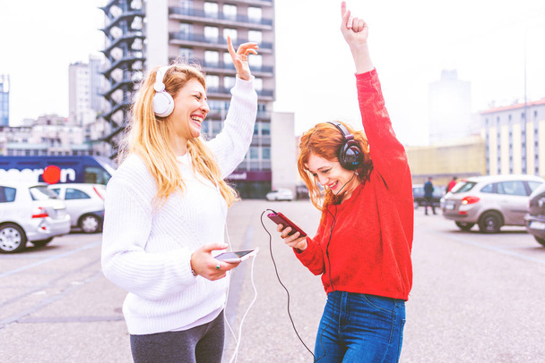 Δύο νεαρές γυναίκες χορεύουν ακούγοντας μουσική με smartphone στην πόλη  - Φωτογραφία, εικόνα