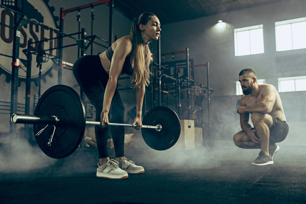 Fit young woman lifting barbells working out in a gym - Foto, imagen