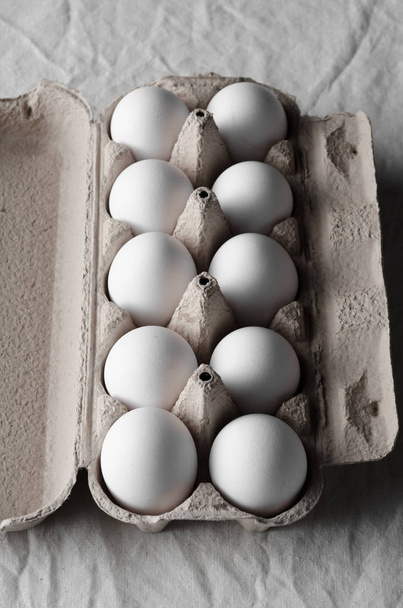 White eggs in an egg carton. White linen tablecloth background. - Фото, изображение