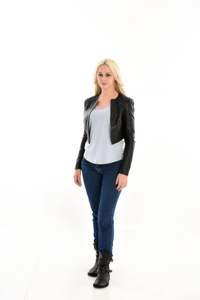 Ganzkörperporträt eines blonden Mädchens in Lederjacke und Jeans. Stehende Pose, isoliert vor weißem Studiohintergrund. - Foto, Bild