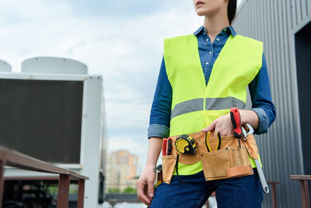 cropped view of female engineer with tool belt in safety vest  - Foto, Bild