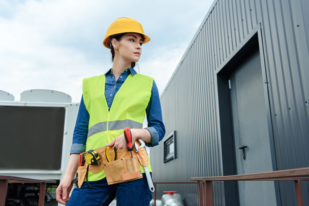 female engineer with tool belt in safety vest and hardhat posing on construction - 写真・画像