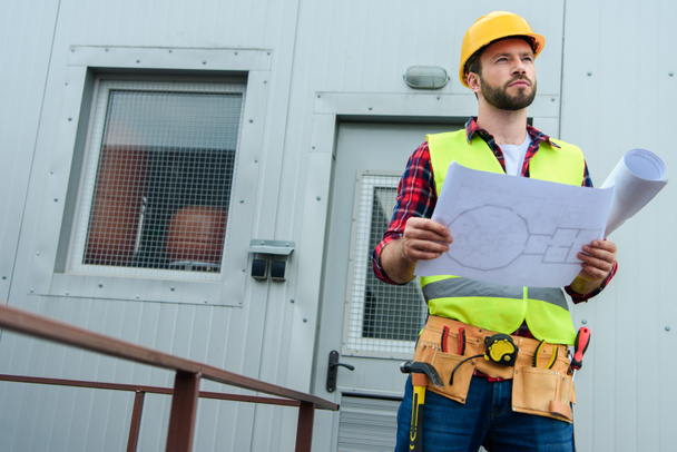male professional engineer in safety vest and helmet working with blueprints - Photo, Image