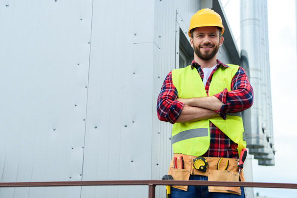 Ingeniero profesional masculino con cinturón de herramientas posando con brazos cruzados - Foto, Imagen