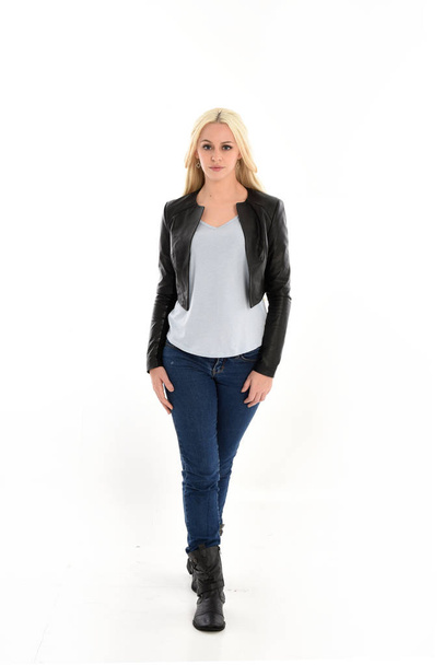 full length portrait o blonde girl wearing leather jacket and jeans. standing pose, isolated against white studio background. - Фото, изображение