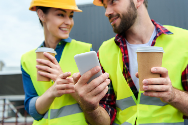 architects in safety vests and helmets using smartphone on coffee break   - Foto, afbeelding