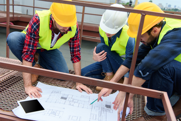 tres ingenieros en chalecos de seguridad y sombreros de trabajo con planos en el techo
 - Foto, Imagen