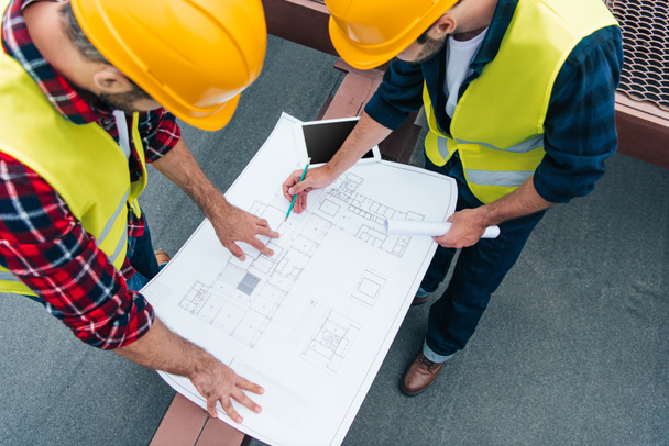overhead view of architects in safety vests and helmets drawing on blueprints - Photo, Image