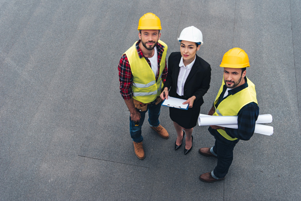 Overhead-Ansicht von Ingenieurinnen und männlichen Arbeitern mit Clipboard und Bauplänen - Foto, Bild