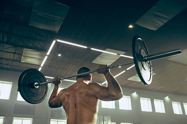 Fit young man lifting barbells working out in a gym - Photo, Image