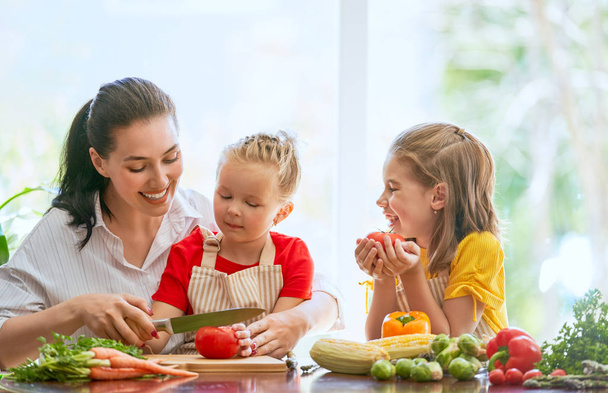 Healthy food at home. Happy family in the kitchen. Mother and children daughters are preparing the vegetables. - Foto, Bild