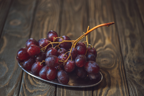 close-up shot of branch of fresh grapes on vintage metal plate on rustic wooden table - Photo, Image