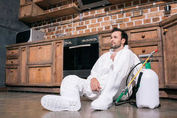 tired pest control worker sitting on floor in kitchen  - Photo, Image