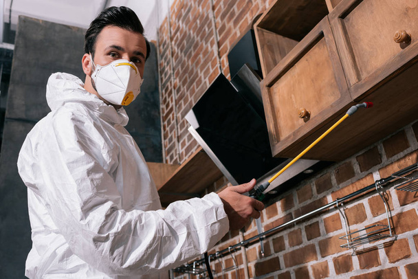 niski kąt widzenia pracownika kontroli szkodników spryskiwanie pestycydami pod półki w kuchni  - Zdjęcie, obraz