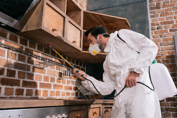 контрольний працівник шкідника обприскує пестициди під полицями на кухні
  - Фото, зображення