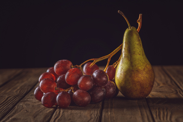 close-up shot of ripe pear and grapes on rustic wooden table on black - Fotó, kép