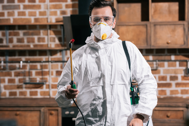 pest control worker standing with sprayer in kitchen and looking at camera - Photo, Image