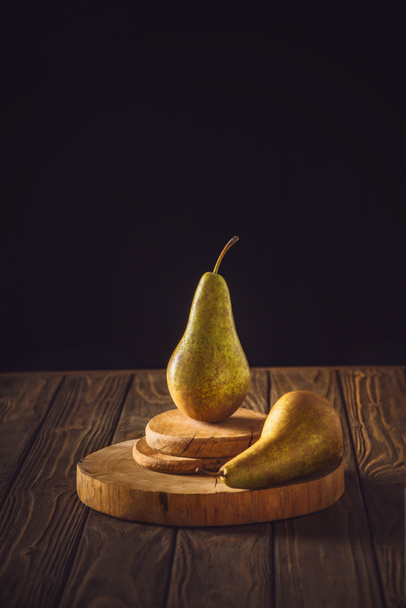 close-up shot of ripe pears on stacked boards and on rustic wooden table on black - Foto, Imagen