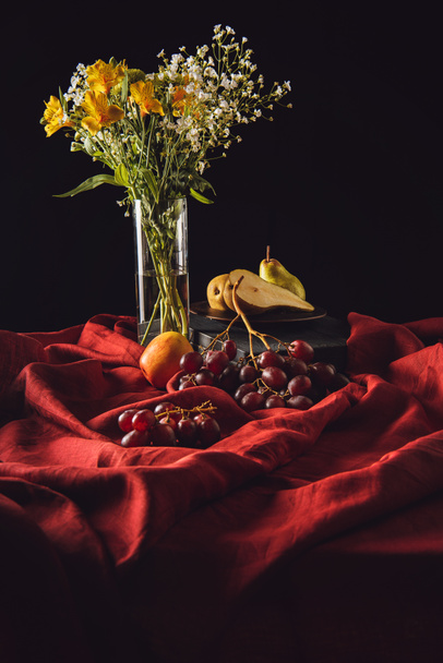 様々 な果物や黒赤カーテンの上に花瓶に花のある静物 - 写真・画像