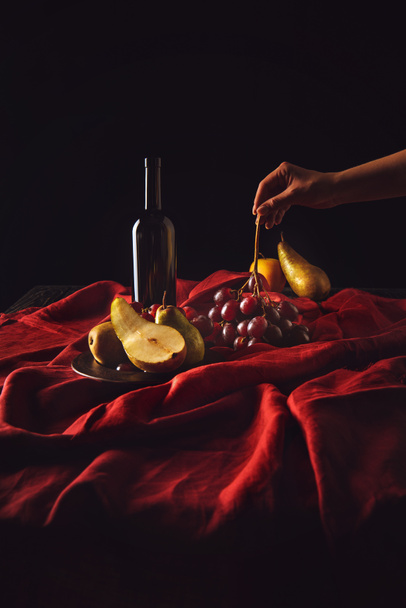 cropped shot of woman taking grapes from table with wine and pears on black - Photo, Image