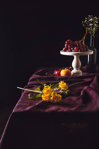 hermosas flores acostadas en la mesa con frutas en el fondo
 - Foto, Imagen