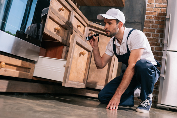 pest control werknemer onderzoeken keuken met zaklamp - Foto, afbeelding