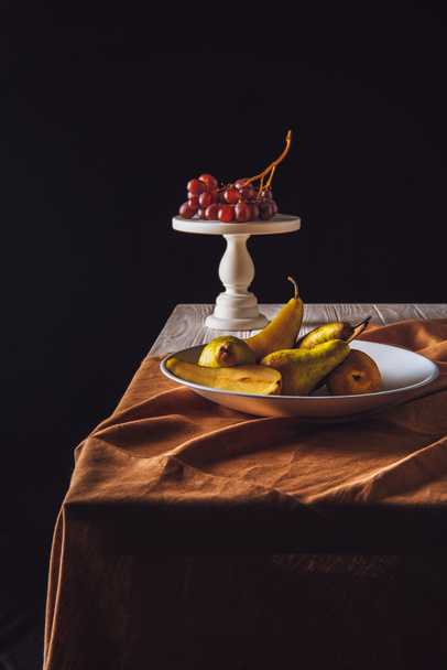 plate of pears and stand with grapes on table on black - Foto, imagen